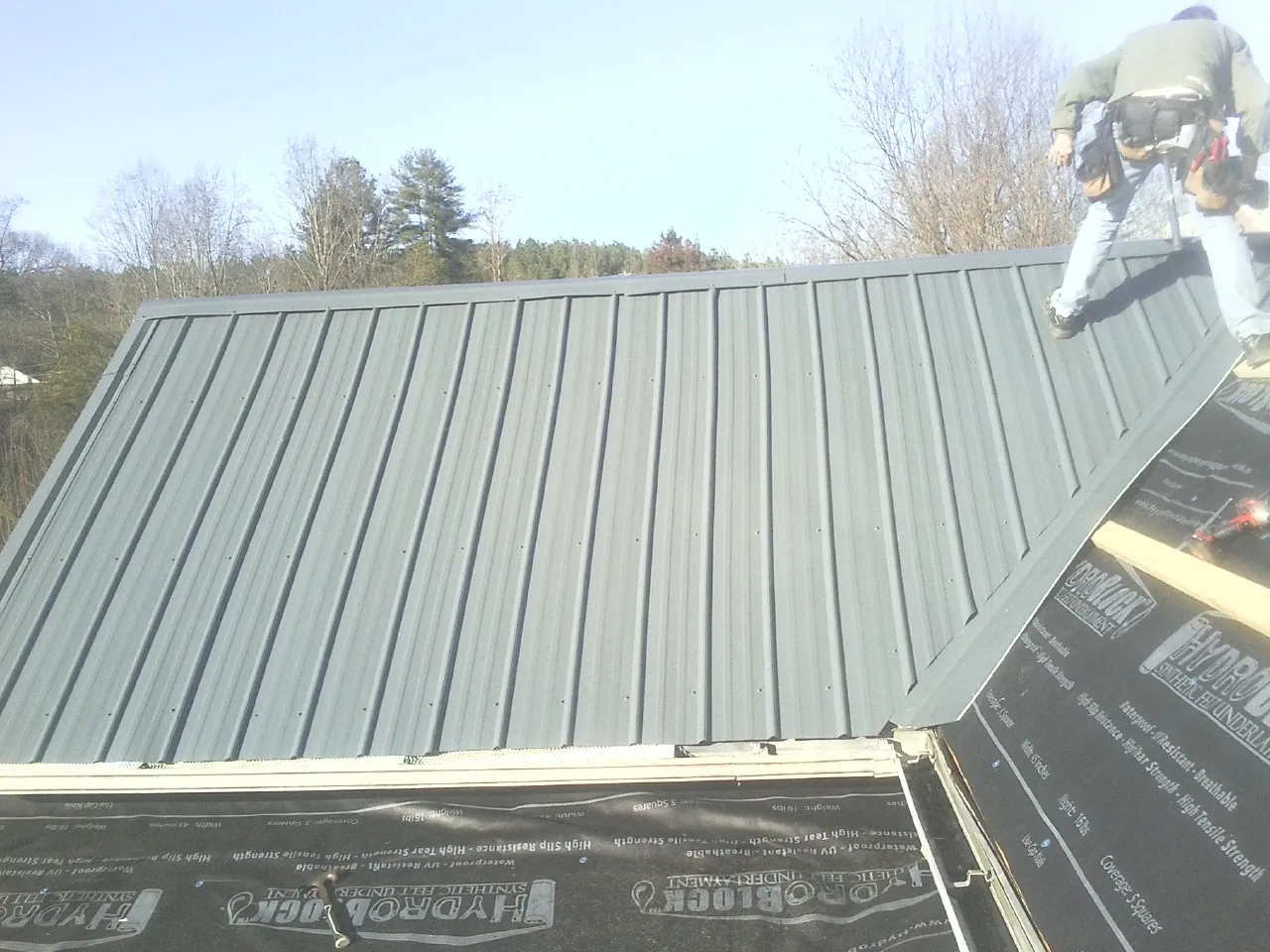 Crew installing dark green standing seam panels over synthetic underlayment in Boston