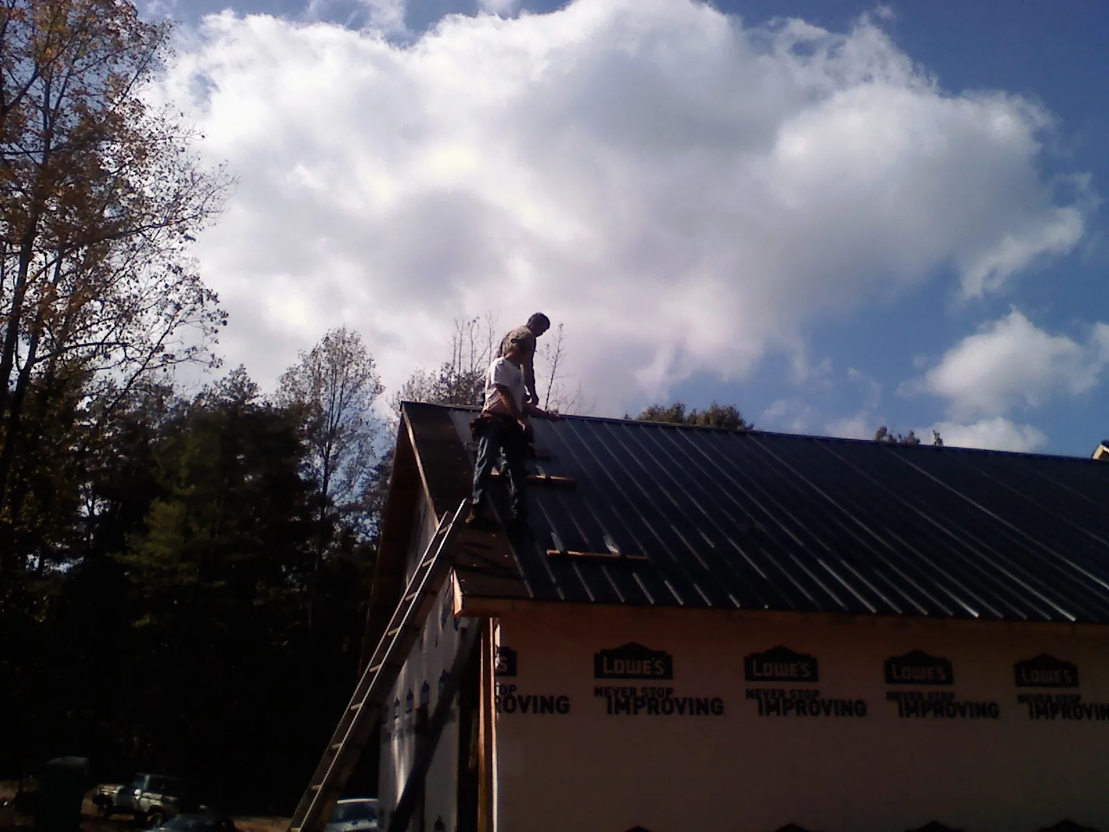 Roofer fastening dark metal panels high against a cloudy sky, from a Roof Inspection job in Boston